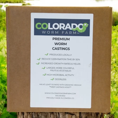 A box labeled "Colorado Worm Farm Premium Worm Castings" sits outdoors, listing benefits such as reduced germination time, increased yields, high microbial activity, and being odorless.